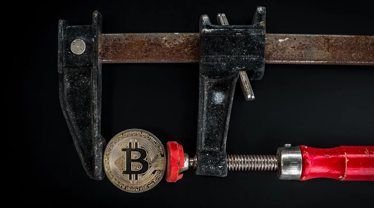 Moneta bitcoin ściśnięta w stolarskim ścisku — zdjęcie ilustracyjne